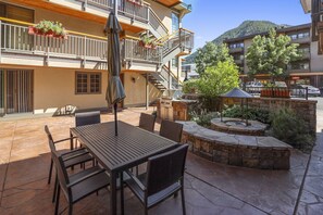 Une terrasse extérieure avec une table et des chaises en bois, un barbecue et un foyer en pierre.
