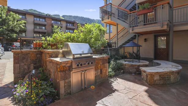 Un espace cuisine extérieur doté d’un barbecue, entouré de murs en pierre et agrémenté de plantes en pot.