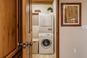 A laundry room with stacked washers and dryers, a wooden door, and a framed artwork on the wall.