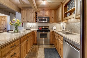 A kitchen with wooden cabinets, stainless steel appliances, granite countertops, and a granite backsplash.