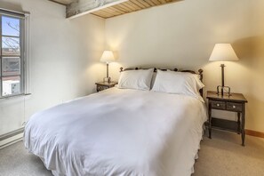 Un lit bien fait, avec du linge de lit blanc, deux tables de chevet avec des lampes et une fenêtre donnant sur les bâtiments environnants.