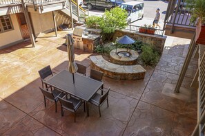Une terrasse extérieure avec une table et des chaises en pierre, un barbecue et un petit arbre.