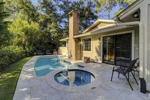 A backyard with a swimming pool, a hot tub, and a patio area with chairs and a bicycle.