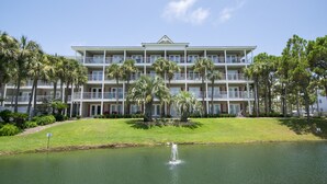 Een meerhoog hotel met een centrale binnenplaats, palmbomen en een kleine vijver met een fontein.