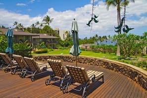 A wooden deck with lounge chairs and umbrellas, surrounded by a stone wall and tropical landscaping.