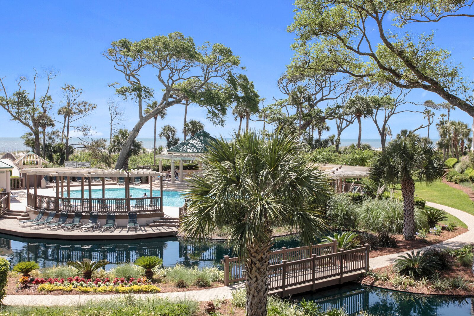 A pool area with lounge chairs, a gazebo, and a palm tree.