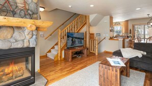 A cozy living room with a stone fireplace, wooden staircase, and a television.