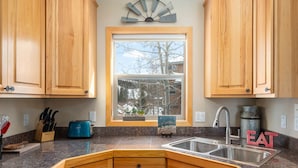 A kitchen with wooden cabinets, a granite countertop, a blue toaster, a sink, and a window with a view of trees.