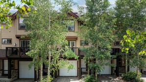 A multi-story residential building with a covered patio area, stone pathway, and lush greenery.