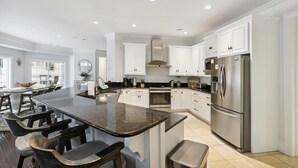 A spacious kitchen with white cabinets, a large island with bar stools, stainless steel appliances, and recessed ceiling lighting. - 3 Surf Watch Way, Pool, Hot Tub, Close To Beach, Free Golf (Hilton Head Island)