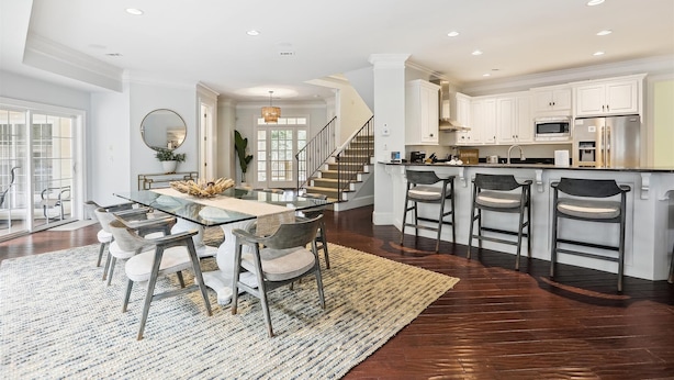 A spacious kitchen with white cabinets, a central island with bar stools, and a dining area with a glass table and chairs. - 3 Surf Watch Way, Pool, Hot Tub, Close To Beach, Free Golf (Hilton Head Island)