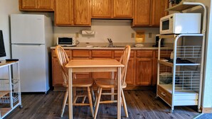 A kitchen with wooden cabinets, a white refrigerator, a microwave, a sink, and a dining table with chairs. - Hotel Style Lodge Room w/Kitchenette (Almont)