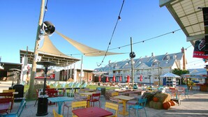Un espace extérieur aménagé en terrasse, avec plusieurs tables et chaises, un grand parasol et un bâtiment en arrière-plan.