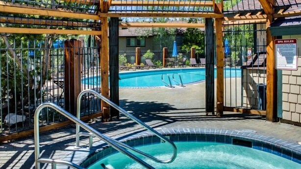 Zona de piscina con un pergolado de madera, escalera metálica para la piscina y un cartel con las normas del spa.