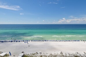 A beach with white sand, clear turquoise water, and a row of blue umbrellas.