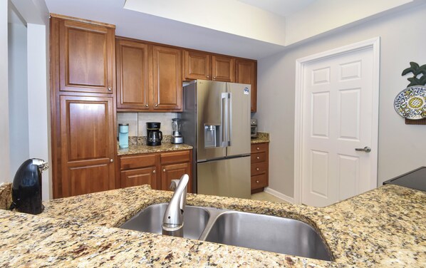 A kitchen with wooden cabinets, a stainless steel refrigerator, a double sink, and a coffee maker.