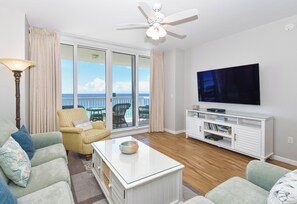 Ein Wohnzimmer mit Fernseher, Deckenventilator und Meerblick durch große Fenster.