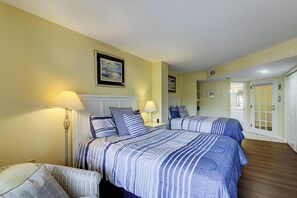 A hotel room with two beds, a wicker chair, and a hallway leading to a bathroom.