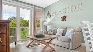 Sala de estar con un sofá, una mesa de centro de madera y vistas al exterior a través de amplios puertas correderas de cristal.