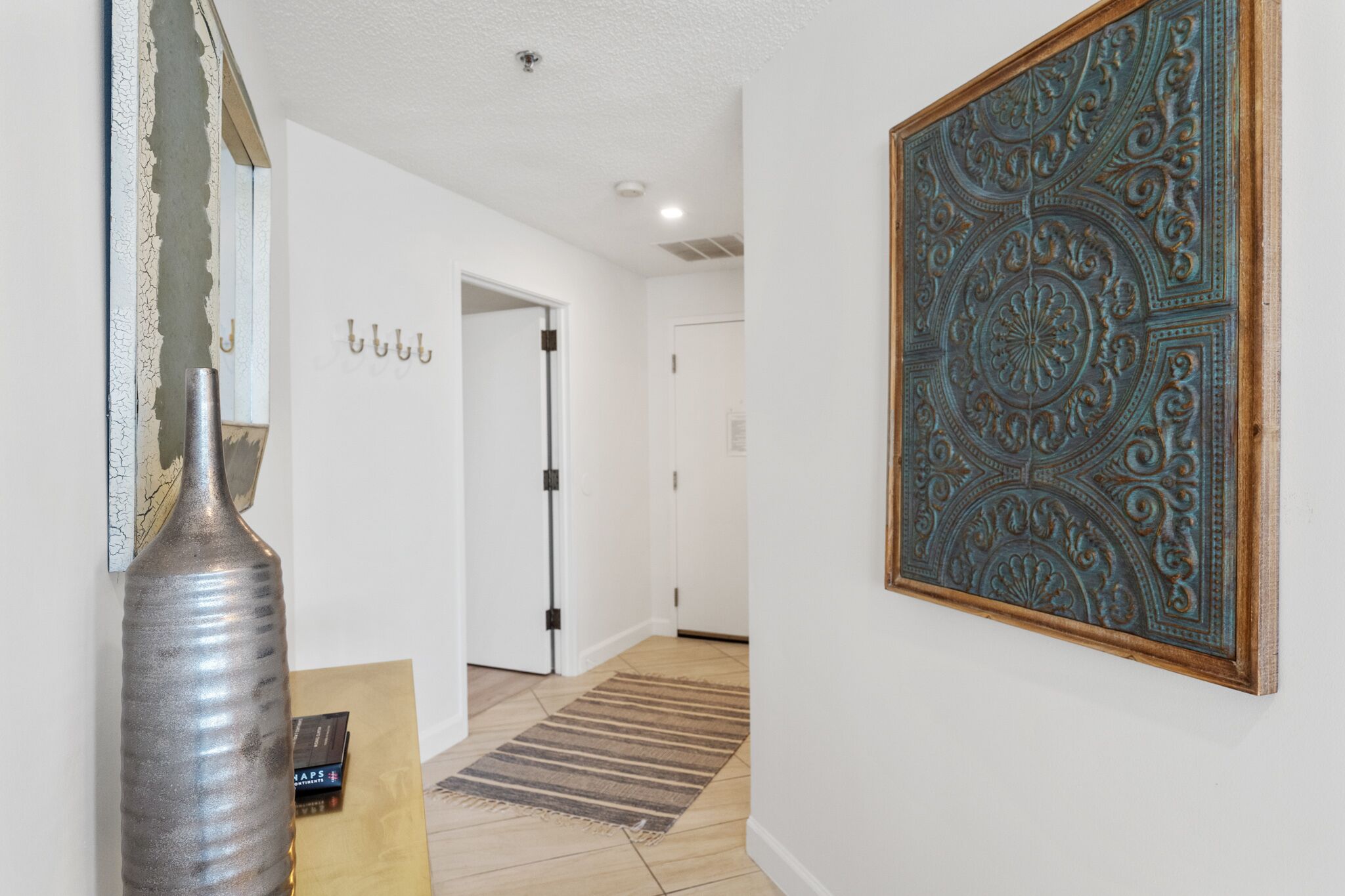 A hallway with a textured wall, a metal sculpture, a patterned wall decoration, and a door.