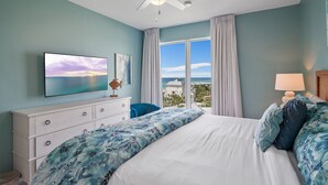 Une chambre avec un grand lit, un ventilateur de plafond, un téléviseur fixé au mur et une vue sur l’océan.