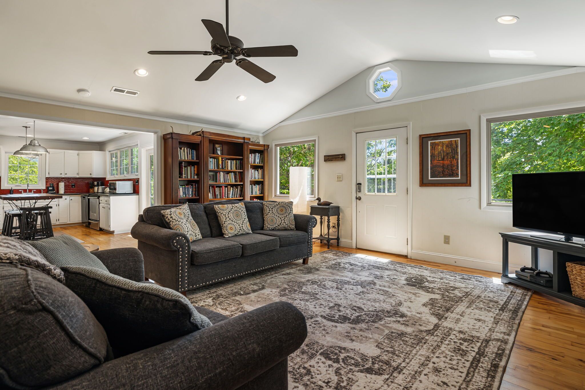 A spacious living room with a dark gray sofa, a large rug, a ceiling fan, and a television.