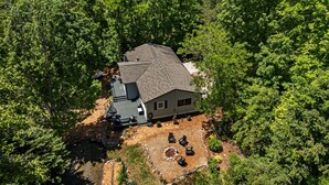 Ein Luftbild eines Hauses, das von dichtem Wald umgeben ist, mit einer Terrasse und einer Sitzgelegenheit im Freien.