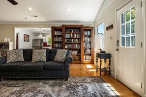 A living room with a dark sofa, a patterned rug, a bookshelf, and a door with a window.