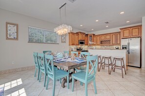 A spacious kitchen with wooden cabinets, a stainless steel refrigerator, and a dining area with turquoise chairs and a wooden table.