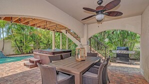 Un patio al aire libre con piscina, jacuzzi, parrilla y ventilador de techo.