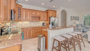 Una cocina con armarios de madera, encimeras de granito, refrigerador de acero inoxidable y una isla integrada con taburetes de bar.