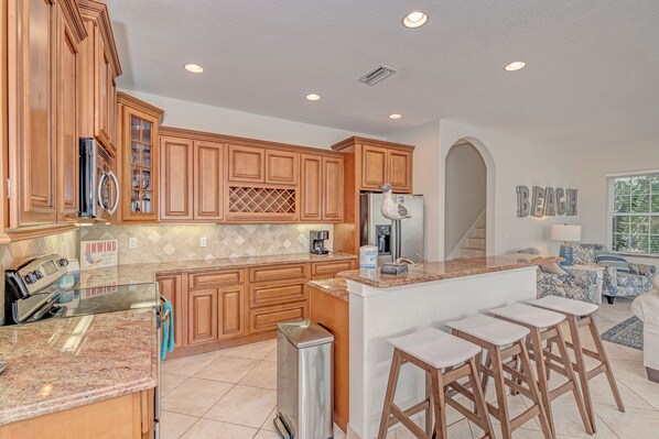 A kitchen with wooden cabinets, granite countertops, a stainless steel refrigerator, and a built-in island with bar stools.