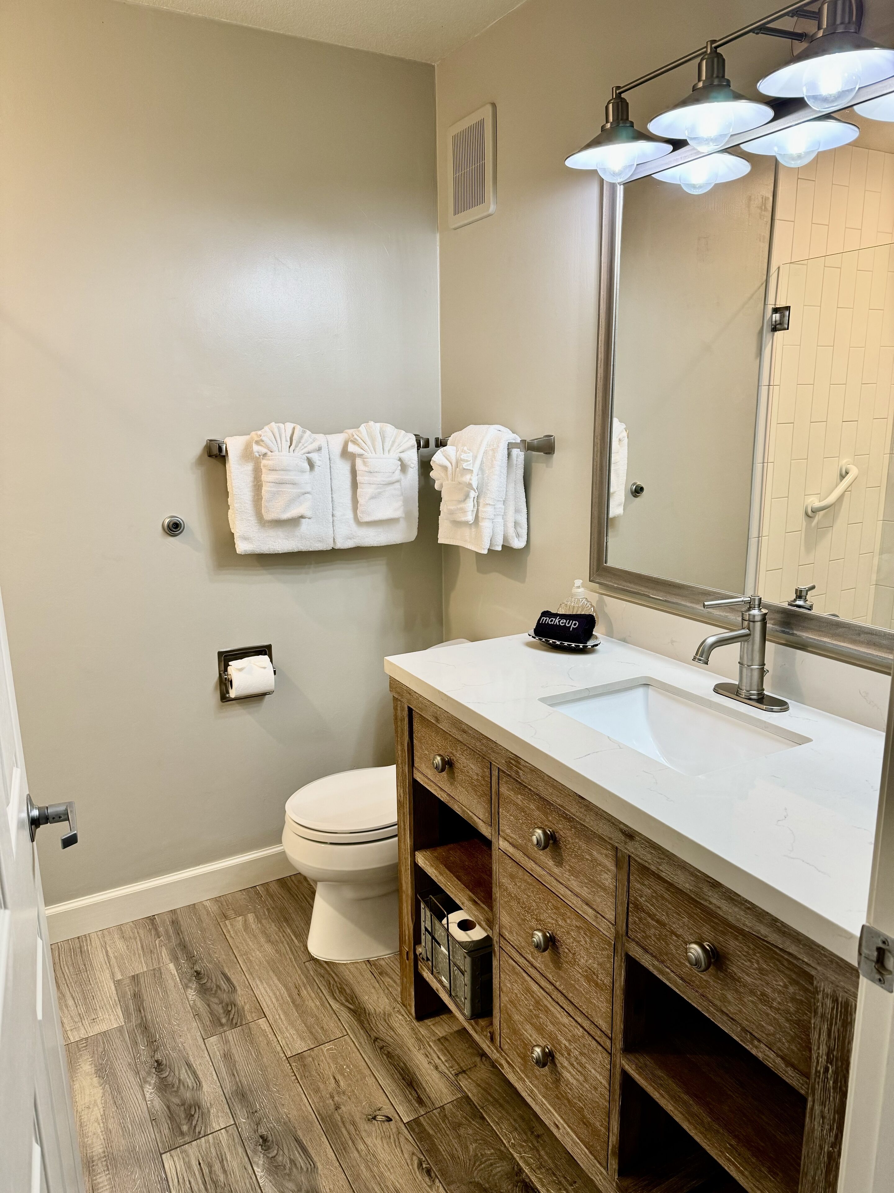 A bathroom with a wooden vanity, a white sink, a mirror, and a toilet.