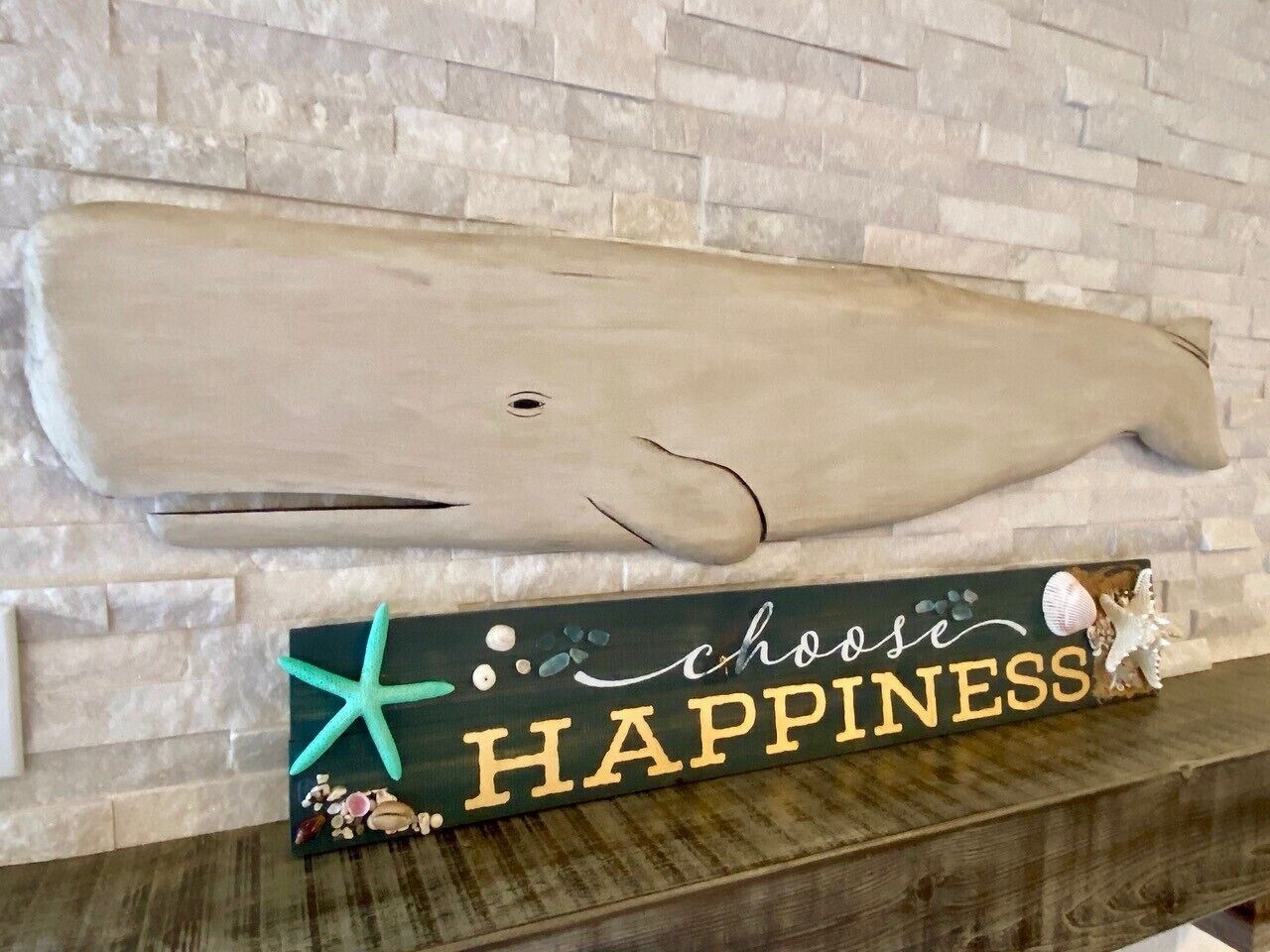 Um letreiro de madeira com as palavras 'chose HAPPINESS' e elementos decorativos como uma estrela-do-mar e conchas.