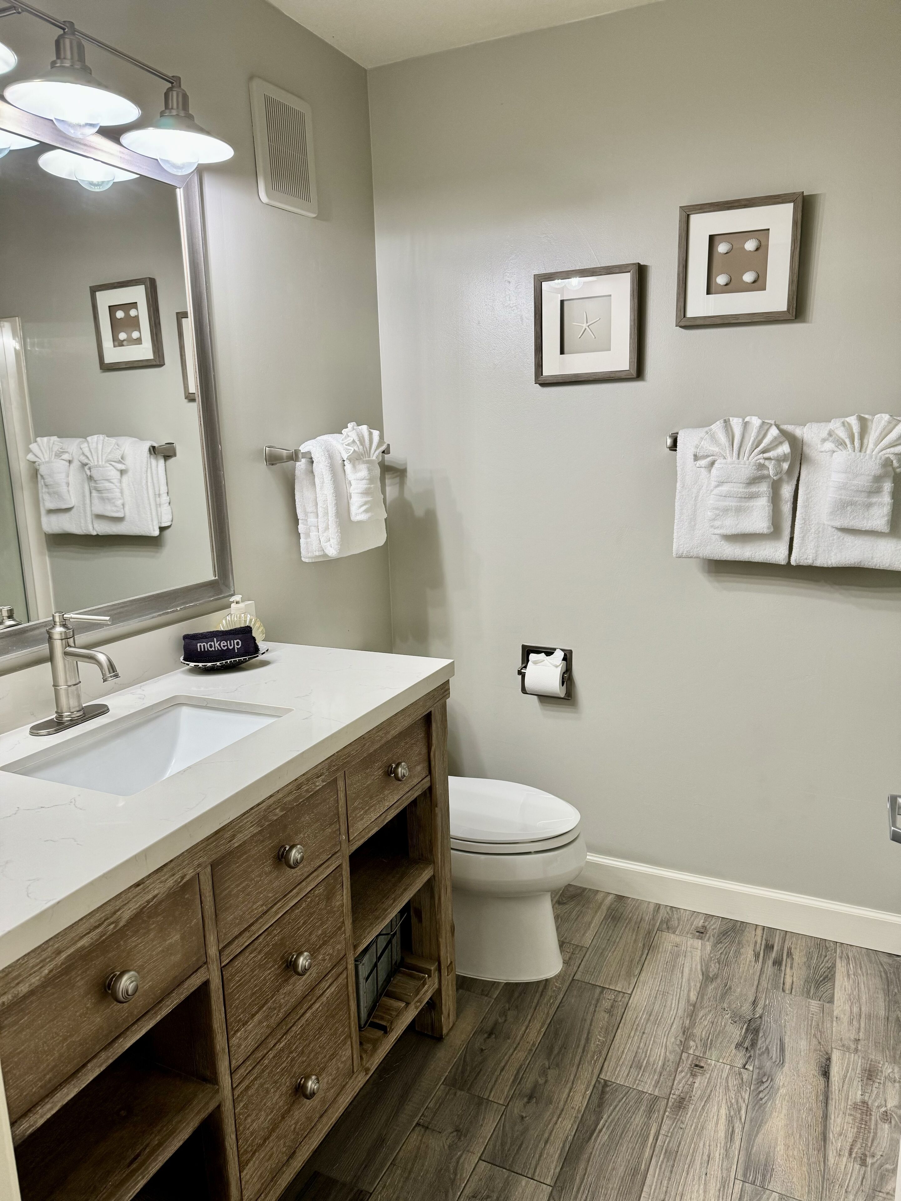 A bathroom with a vanity, sink, mirror, towel racks, and a toilet.