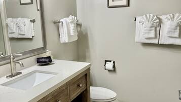A bathroom with a vanity, sink, mirror, towel racks, and a toilet.