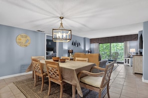 A dining area with a wooden table and chairs, a chandelier, and a view of the outdoors.