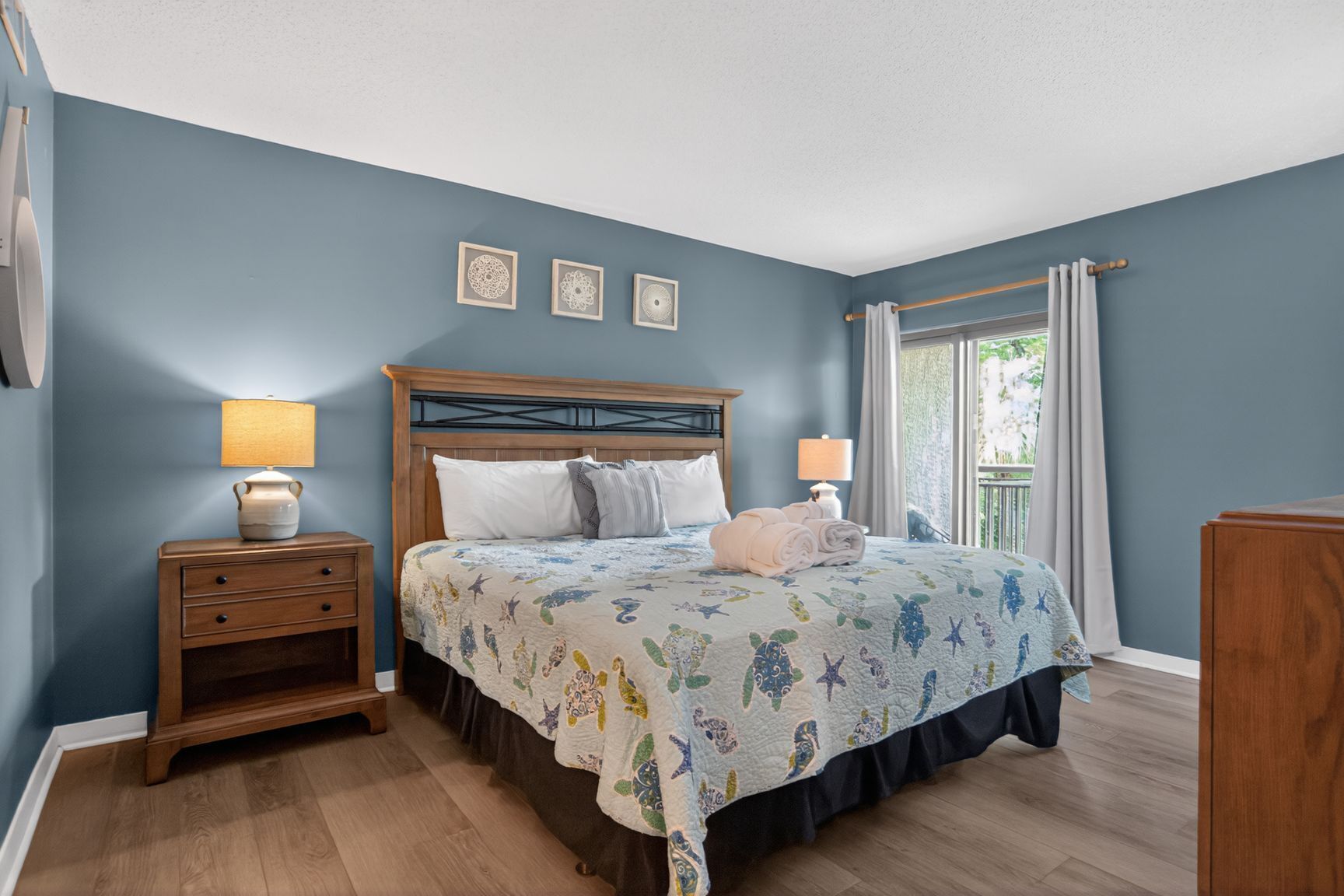 A bedroom with a bed, nightstands, a window with curtains, and wall art.