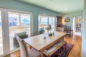 A dining area with a wooden table and wicker chairs, overlooking a beach.