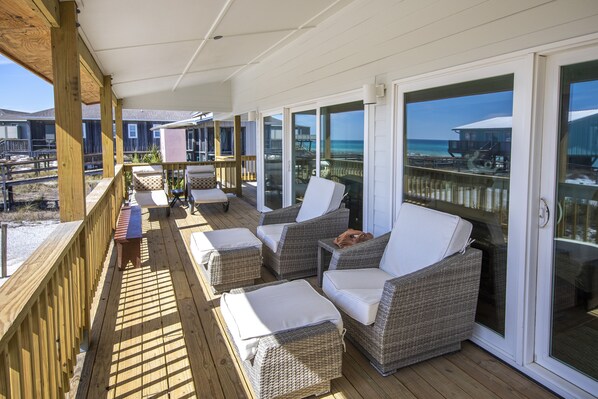 A covered outdoor deck with wicker furniture and a view of the beach and ocean.