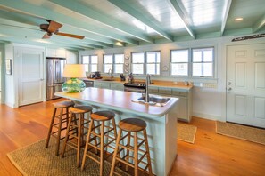 A kitchen with a central island, bar stools, a refrigerator, and a ceiling fan.
