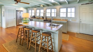A spacious kitchen with a central island, wooden stools, a refrigerator, and a ceiling fan. - One Lot From Beach, Gulf View, Private Beach Boardwalk, Dune Allen Beach (Santa Rosa Beach)