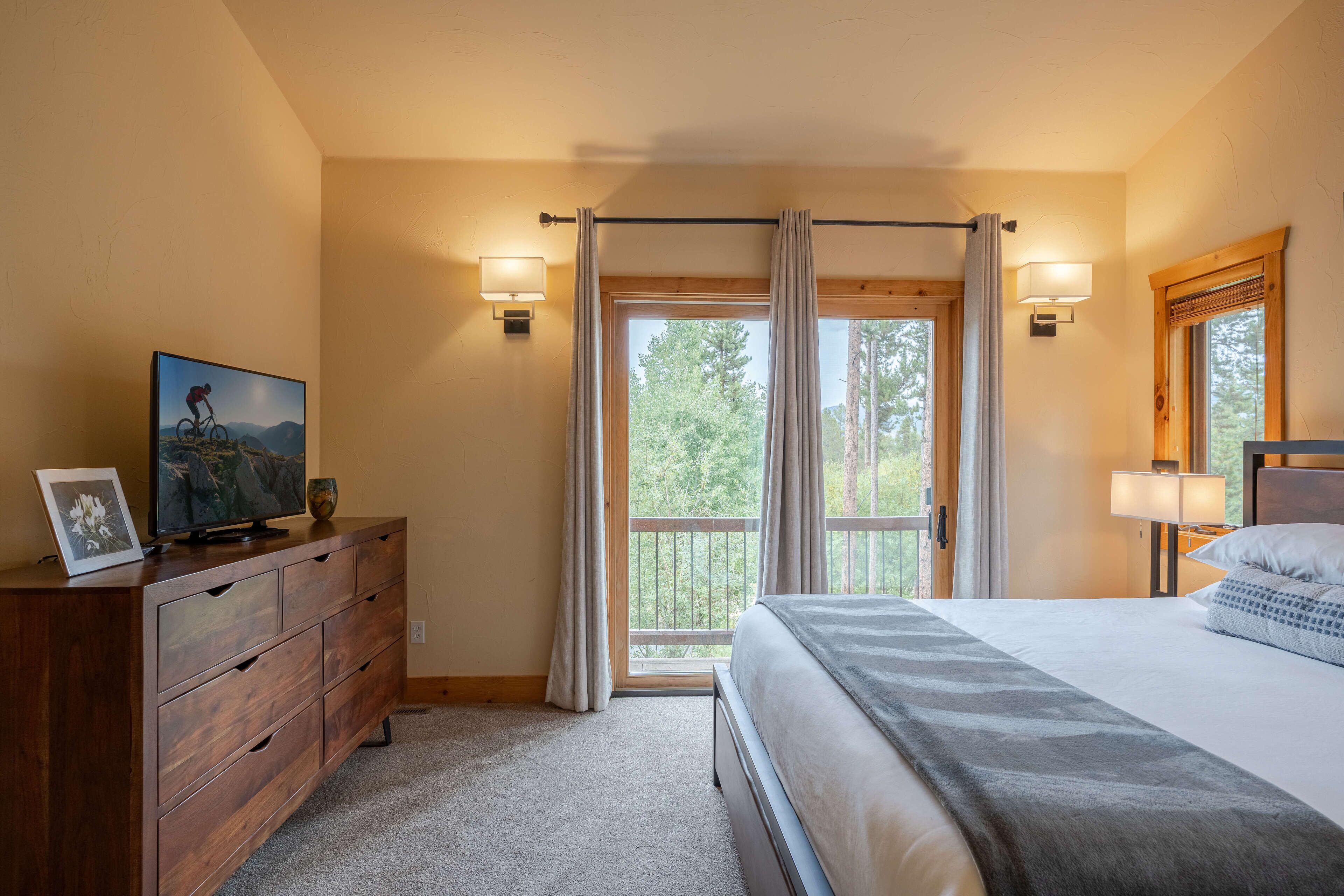 Une chambre à coucher avec un lit, une commode, un téléviseur et une fenêtre avec des rideaux.