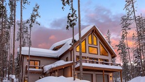 A two-story lodge with a snow-covered roof, large windows, and a balcony.