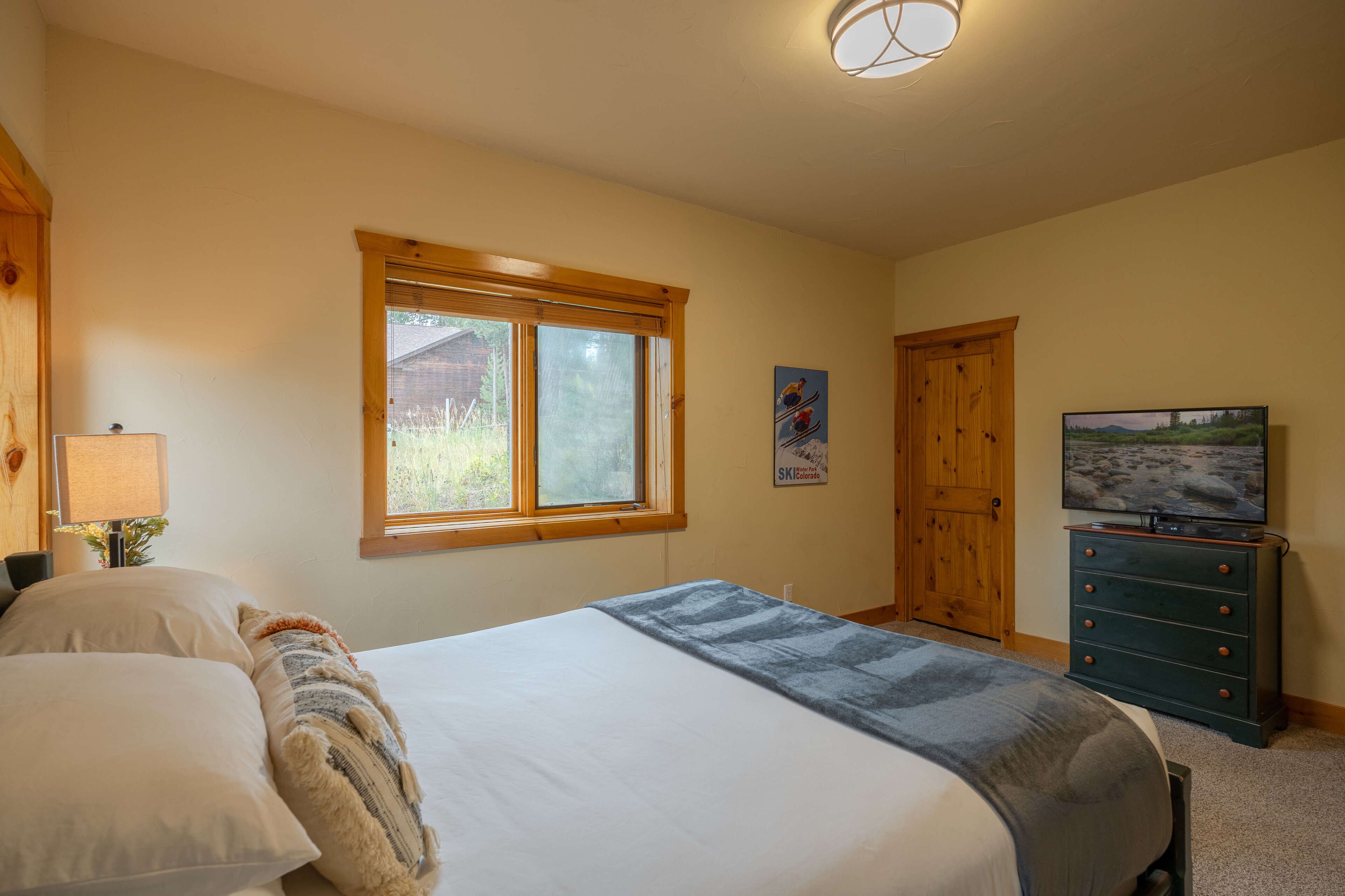 A bedroom with a large bed, a wooden wardrobe, a television, and a window with a view of the outdoors.