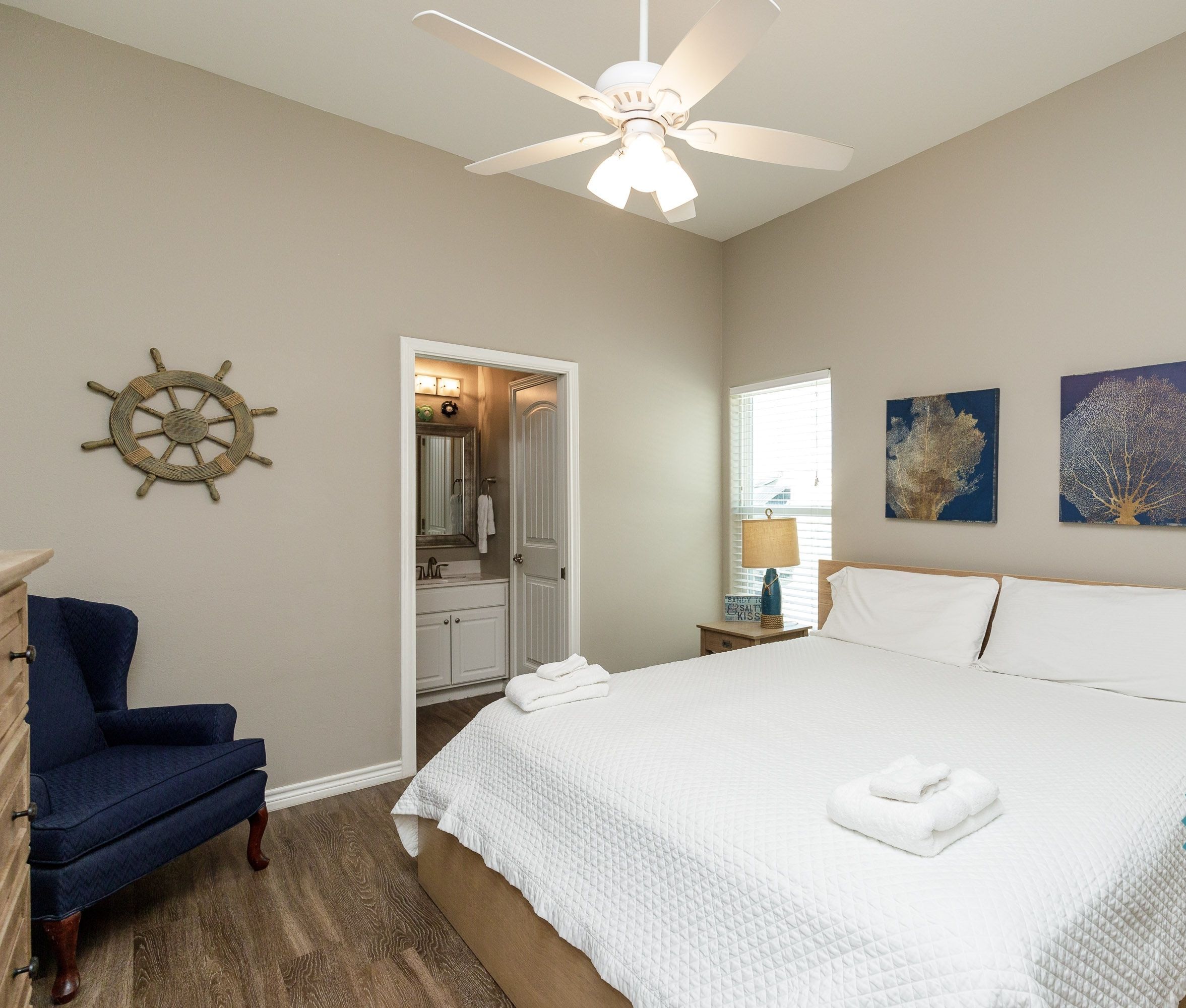 A clean, well-lit bedroom with a large bed, a ceiling fan, and artwork on the walls.