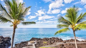 A beach with two palm trees, a wooden bench, and a rocky shoreline. - Aloha Condos, Keauhou Kona Surf and Racquet Club, Condo 1-306, Oceanfront (Kailua Kona)
