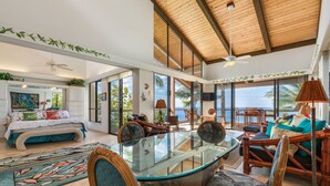 A spacious living area with a glass dining table, comfortable seating, and large windows offering ocean views. - Aloha Condos, Keauhou Kona Surf and Racquet Club, Condo 1-306, Oceanfront (Kailua Kona)