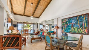 A spacious living area with a high ceiling, large windows, and a tropical-themed mural. - Aloha Condos, Keauhou Kona Surf and Racquet Club, Condo 1-306, Oceanfront (Kailua Kona)