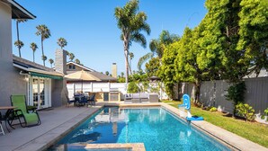 Una piscina rectangular con una terraza empavedada, rodeada de palmeras y una cerca de madera.